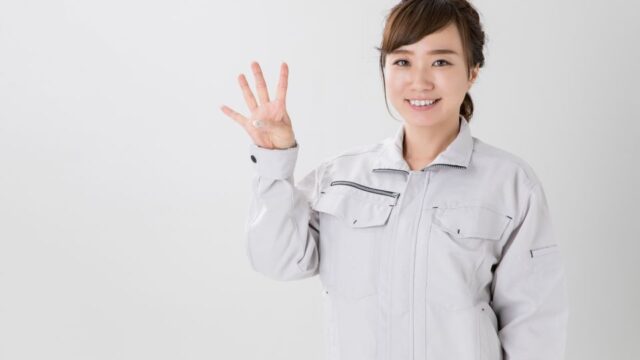 指で4の数字を表す作業服を着た女性の画像